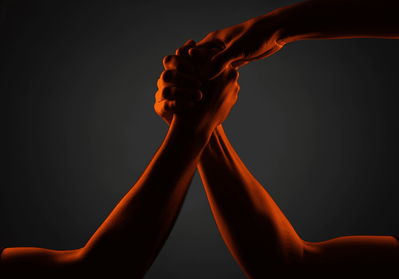 One hand pulling another upward in ember light